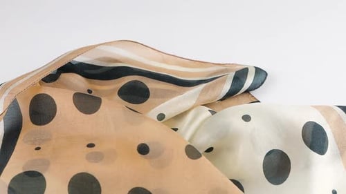 A light beige thinnest scarf made of natural silk with black polka dots falls in soft folds slowly