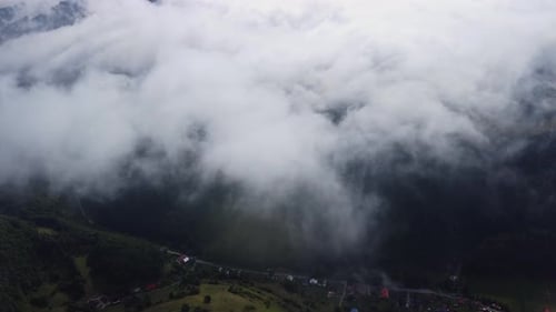 Misty Fog Blows Over the Mountain Landscape Road and Dwellings Under the Clouds