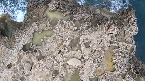 Aerial top view of two tourists on natural shaped rocks in Dwejra Bay, maltese island of Gozo. Medit