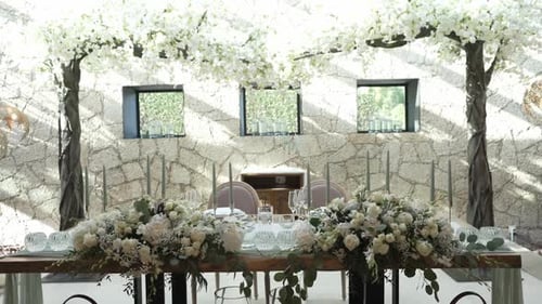 Elegant wedding table setup with floral arrangements and candle decor under white blossom arches