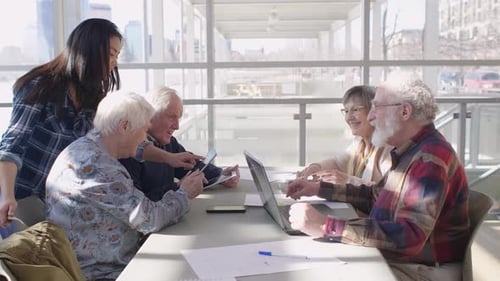 Young Woman Helps Seniors with Technology at Table