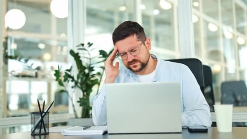 Man with Headache at Desk in Bright Office