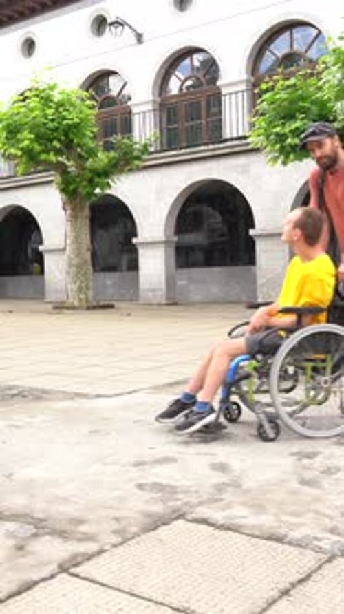 A disabled person in a wheelchair walking through the town square with a friend
