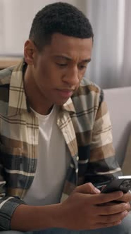 Thoughtful Young Man Using Mobile Phone Indoors