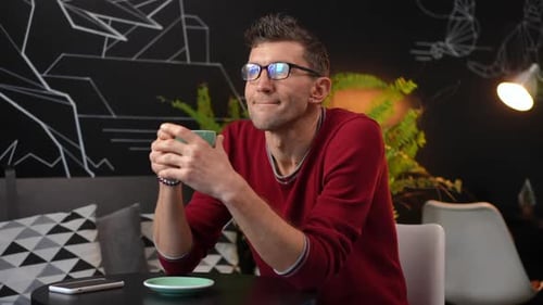 Portrait of Thoughtful Caucasian Man in Eyeglasses Sitting with Coffee Cup in Cafe Looking Away