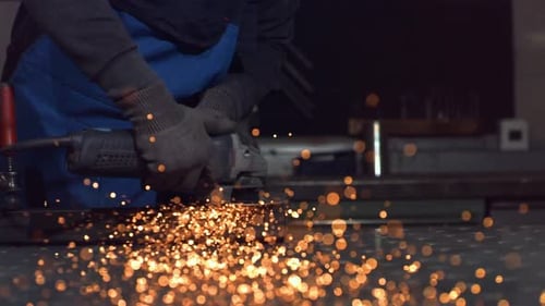 Metalworker Grinding Steel with Sparks in Dark Workshop
