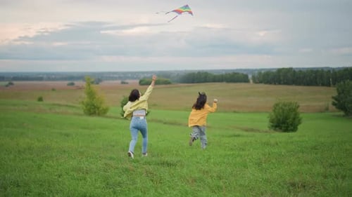 Two Girls Running with Kite in Grassy Field