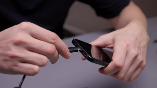 Manos que sostienen el teléfono inteligente negro y el cable USB a punto de conectarse al puerto, simbolizando los datos de carga