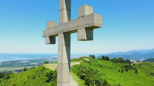 Close-up view from drone of Orthodox cross on mountain against sea against sun,