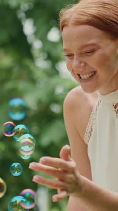 Woman Playing with Colorful Bubbles Outdoors in a Lush Garden Setting