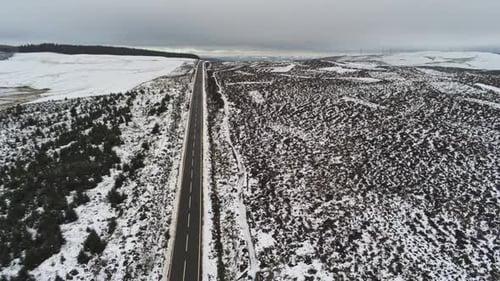 Long road aerial into distance across highland snowy countryside moors high to low