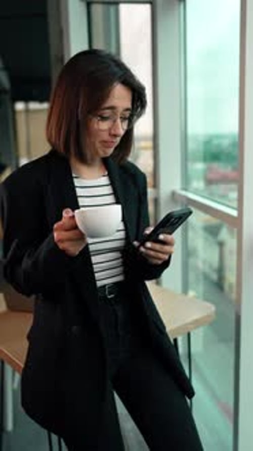 Business lady surfing internet and drinking coffee. Woman uses her smartphone during a lunchbreak.