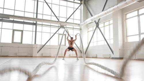 Intense Man Working Out with Battle Ropes in Gym