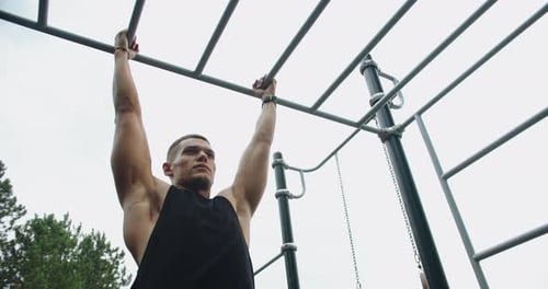Athletic Man Hanging on Horizontal Bars Outdoors