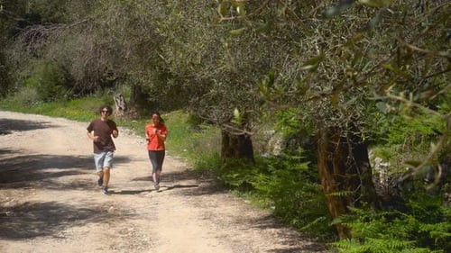 couple of young fitness athletes running on country road in a woodland. Slowmotion