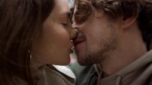 Affectionate young couple kissing and touching noses on urban street in spring day