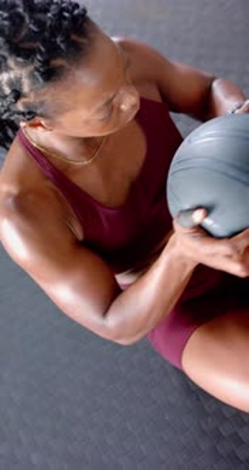 Vertical video: Using medicine ball, woman doing core workout on gym floor, focused on fitness