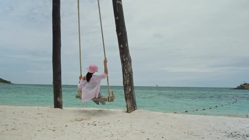 Woman is sitting and swinging on a swing on the beach in island and the sea.