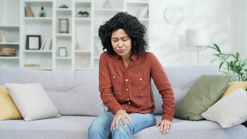 Woman Rubs Knee in Pain on Couch