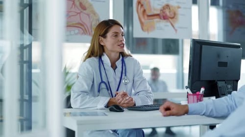Smiling Doctor Woman Sitting at Table in Medical Office Speaking with Man Patient During