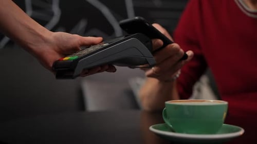 Closeup Unrecognizable Waitress with POS Terminal in Cafe and Man Paying with Smartphone Application