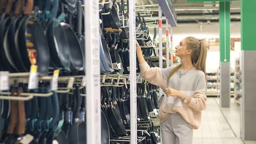 Une jeune fille choisit une nouvelle poêle pour sa cuisine dans un grand supermarché