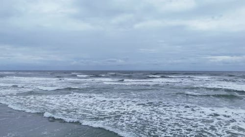 Scenic Wide Shot of Strong Waves Rolling Toward Coastline on a Cloudy Day