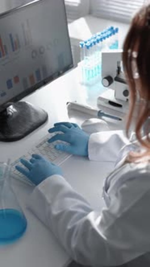 Scientist Typing at Desk with Microscope and Test Tubes