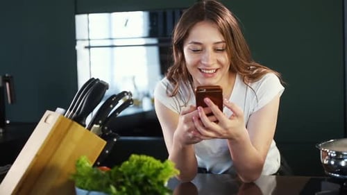 Smiling Woman Using Phone in Modern Kitchen