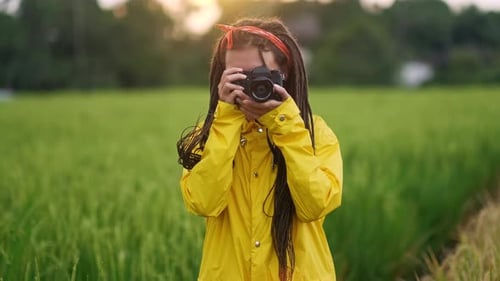 Young Photographer with Dreadlocks and Yellow Raincoat Taking Pictures in a Green Field