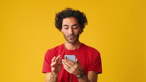 Smiling man using mobile phone, scrolling application isolated on yellow background in studio