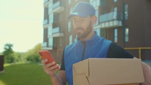 At Sunlight Smiling Handsome Young Man Delivery Texting Message on Smartphone Outdoor and Looking
