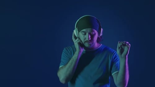 A Man Wearing White Wireless Headphones Listens to Music and Dances A Man in a Studio on a Blue