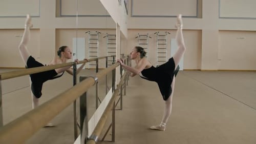 Female Ballerina Exercises at Barre in Dance Studio
