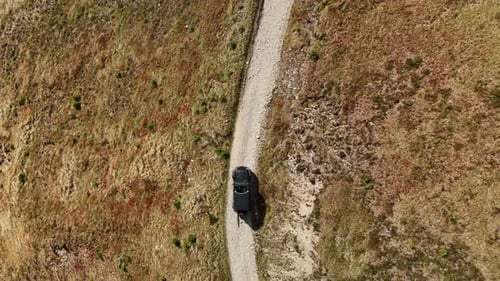 SUV driving down a narrow dirt road surrounded by dry, rugged landscape on a sunny day