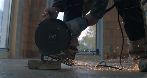 Worker using angle grinder on concrete block, sparks fly in industrial construction task, hands-on