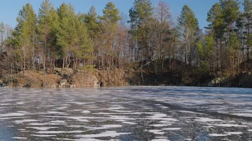 A frozen lake with a textured icy surface reflects the clear blue sky. Surrounding it tall evergreen