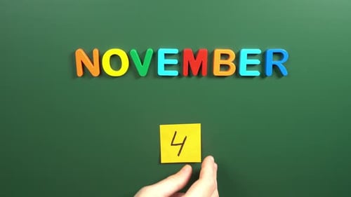 Hand sticking a sticker 4 November calendar day on school board. 4 date of November. Fourth day