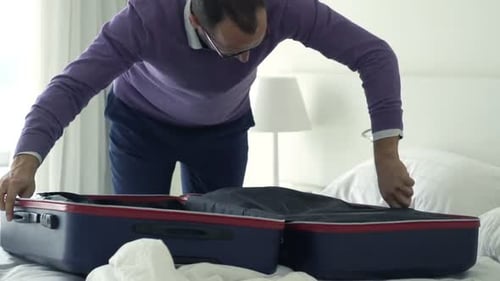 Man packing suitcase on bed in hotel room
