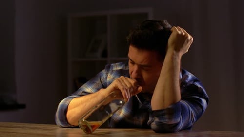 Distraught man drinks alcohol at a table