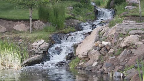 Water rapidly flowing from small cascade waterfall into pond in park
