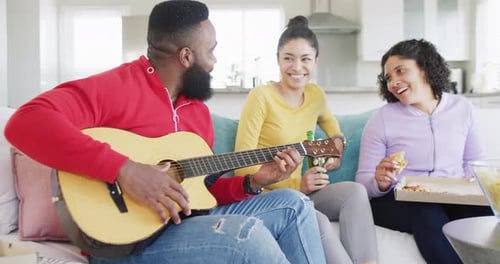 Happy, diverse female and male friends playing guitar and listening at home in slow motion