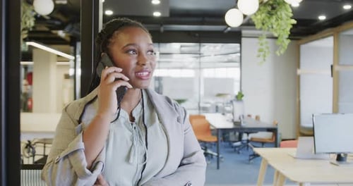 Happy african american casual businesswoman talking on smartphone standing in office, slow motion