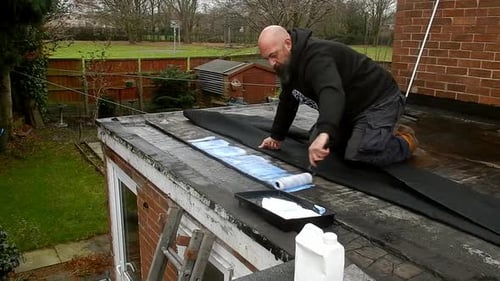 Man Paints Roof with Roller and Blue Liquid