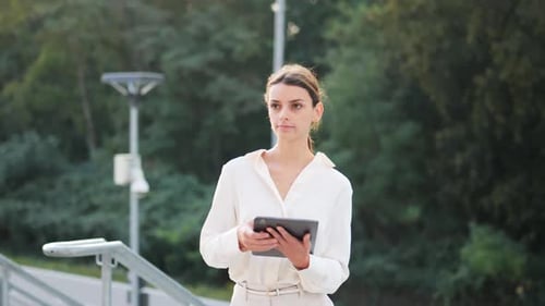 Young attractive businesswoman walks up the stairs with a tablet in her hand