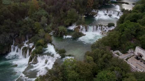 Aerial view of lush waterfall and river in serene forest, Croatia.
