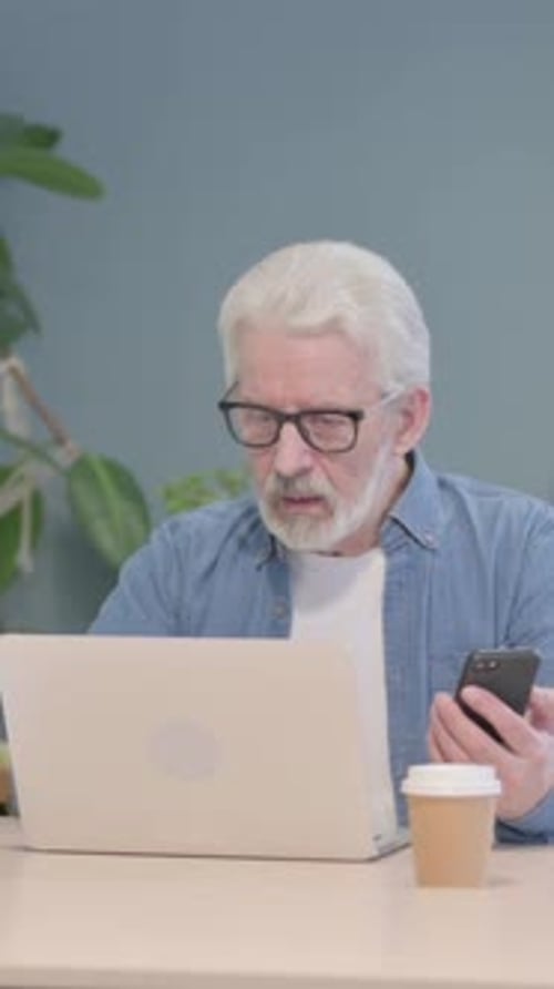 Senior Man Uses Laptop and Mobile Device at Table