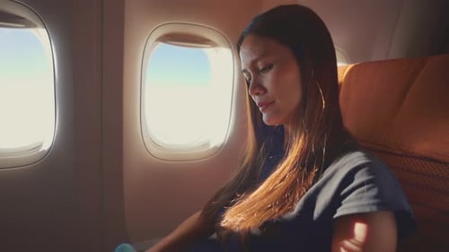 Asian woman put on headphone listen to music while sitting in airplane.