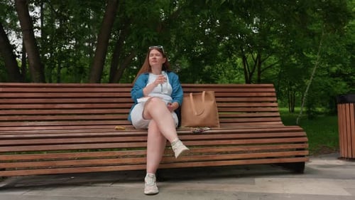 Young Girl Enjoying Park Serenity While Sipping Water on Wooden Bench