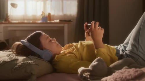 Girl with Headphones Lies in Bed, Using Phone